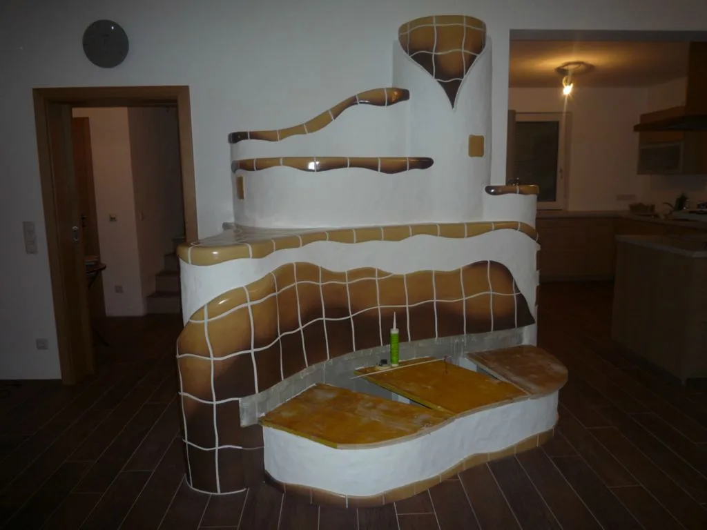 Ofen mit gelber Handkeramik und geschwungener Liegefläche vor einer Treppe