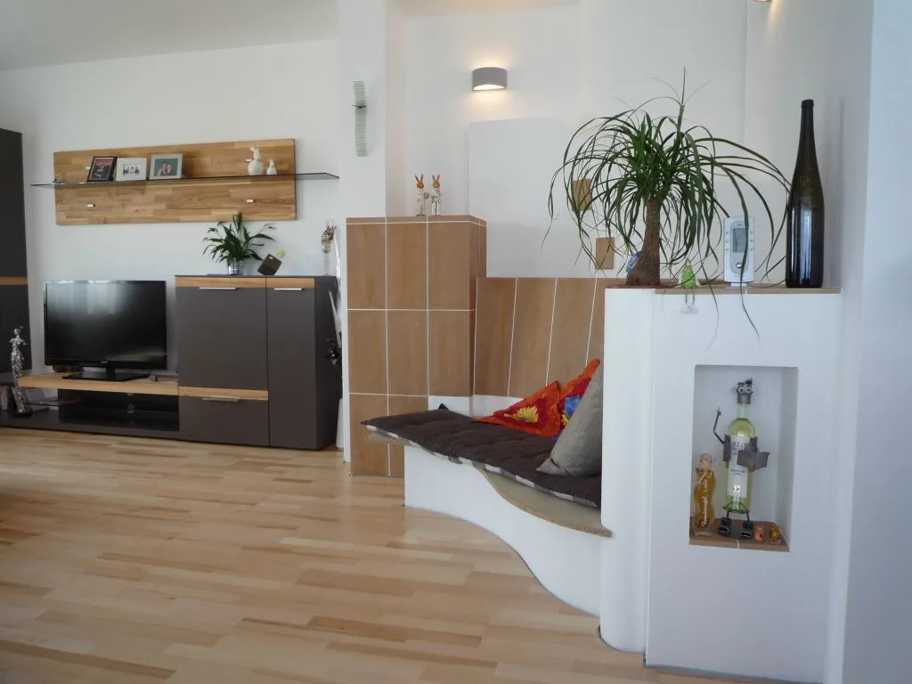 Kachelofen als Raumteiler mit langer gepolsterter Sitzbank neben einem Wohnzimmer